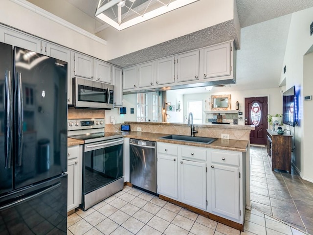 kitchen with white cabinetry, kitchen peninsula, appliances with stainless steel finishes, tasteful backsplash, and sink