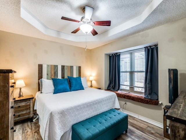 bedroom featuring a textured ceiling, ceiling fan, dark hardwood / wood-style flooring, and a tray ceiling