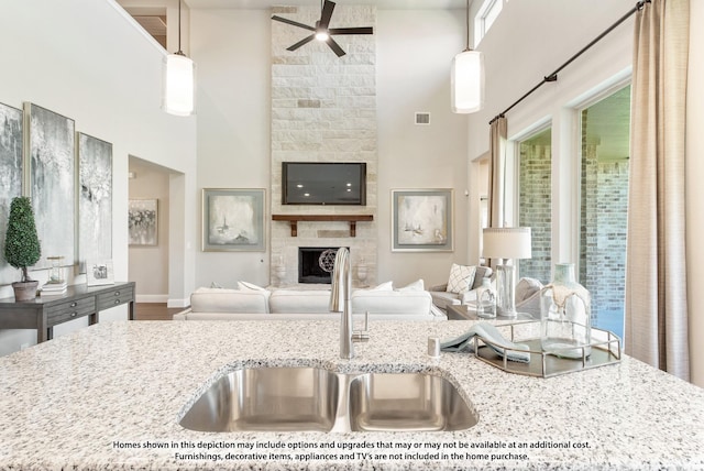 kitchen with light stone countertops, decorative light fixtures, a fireplace, sink, and ceiling fan