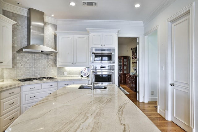 kitchen featuring hardwood / wood-style flooring, white cabinetry, stainless steel appliances, light stone countertops, and wall chimney exhaust hood