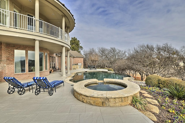 view of patio with a swimming pool with hot tub and a balcony