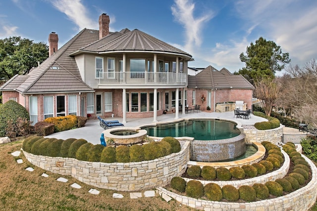 back of property with a patio, a balcony, and a pool with hot tub