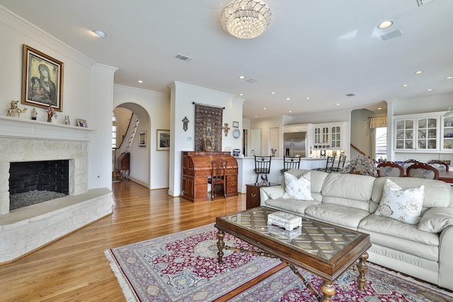 living room featuring a stone fireplace, a wealth of natural light, ornamental molding, and light wood-type flooring