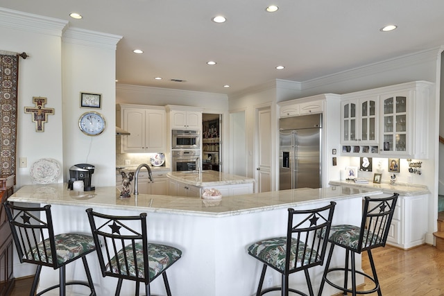 kitchen with a breakfast bar, white cabinetry, light wood-type flooring, kitchen peninsula, and stainless steel appliances