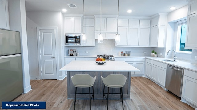 kitchen with decorative light fixtures, a center island, sink, white cabinetry, and stainless steel appliances