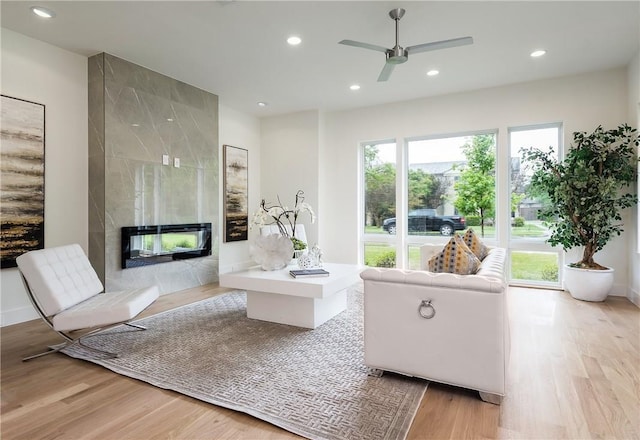 living room with light wood-type flooring, ceiling fan, and a high end fireplace