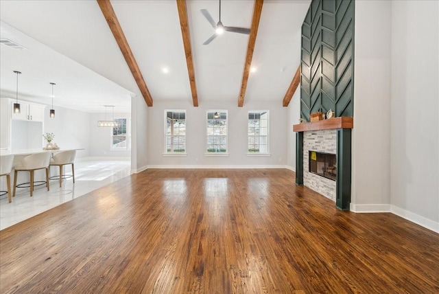 unfurnished living room featuring ceiling fan, a large fireplace, dark hardwood / wood-style flooring, and lofted ceiling with beams