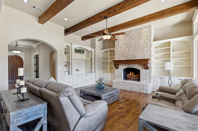 living room featuring ceiling fan, dark hardwood / wood-style floors, a fireplace, built in shelves, and beamed ceiling