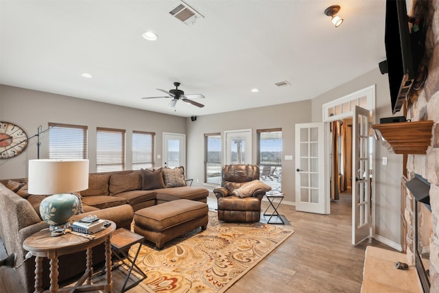 living room with light hardwood / wood-style floors, ceiling fan, a stone fireplace, and french doors