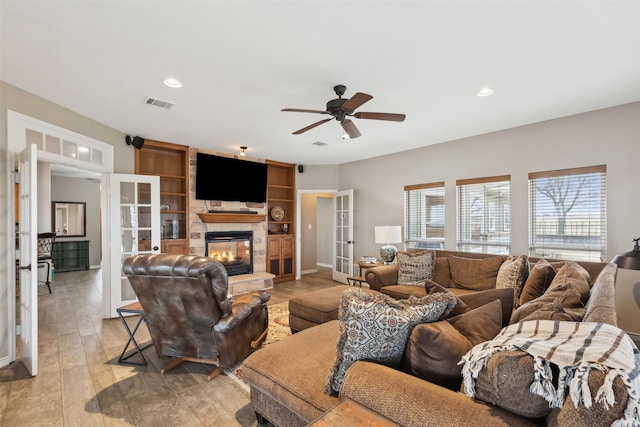 living room featuring light wood-type flooring, french doors, a stone fireplace, and ceiling fan