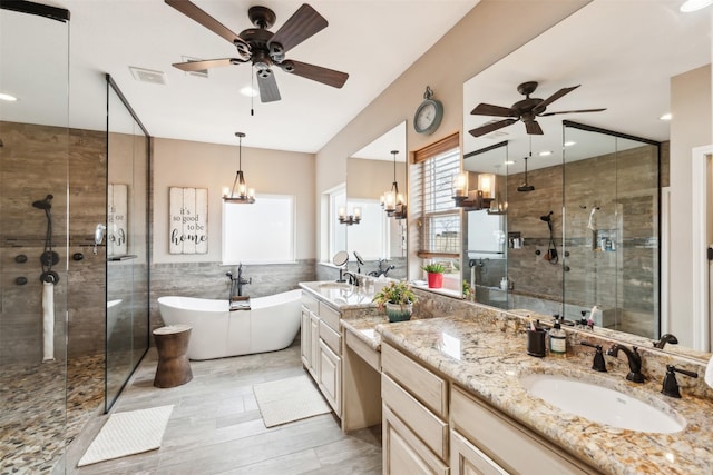 bathroom with ceiling fan with notable chandelier, tile walls, vanity, and separate shower and tub