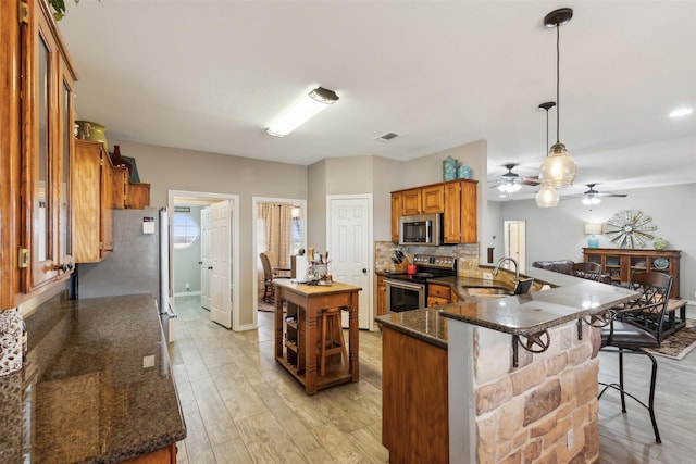 kitchen featuring kitchen peninsula, sink, hanging light fixtures, light wood-type flooring, and stainless steel appliances