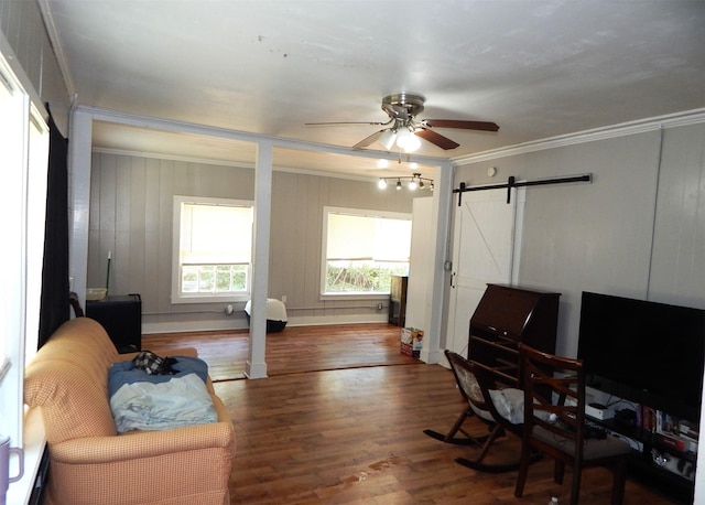 living area with ceiling fan, wood-type flooring, crown molding, and a barn door