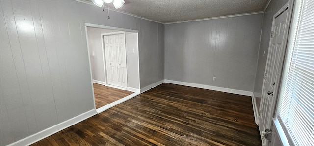 unfurnished bedroom with a textured ceiling, dark wood-type flooring, ornamental molding, and wooden walls