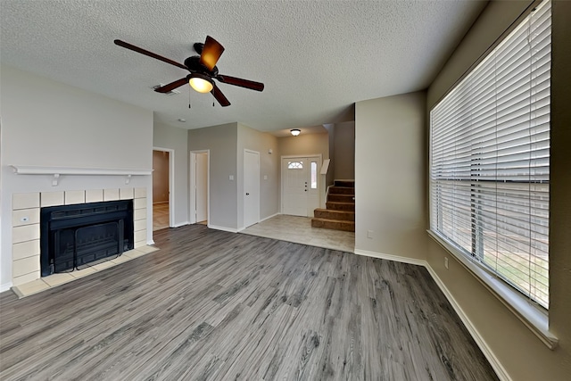 unfurnished living room with a fireplace, a textured ceiling, ceiling fan, and light wood-type flooring