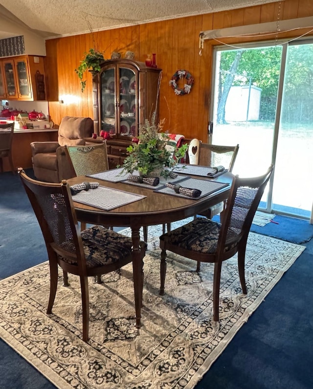 carpeted dining space with a textured ceiling and wood walls