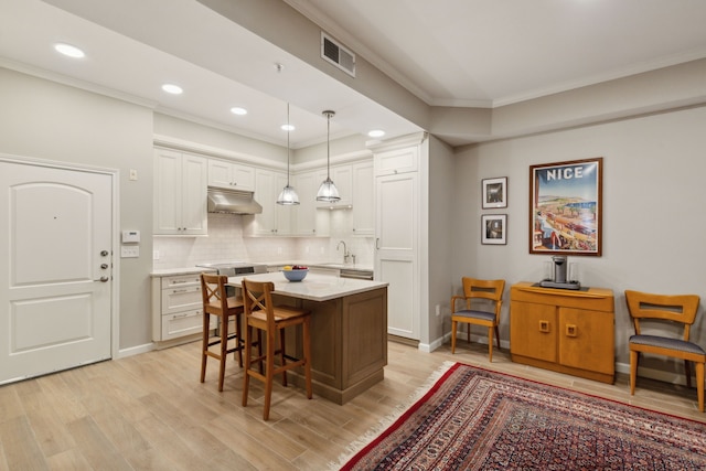 kitchen featuring decorative light fixtures, white cabinets, a kitchen island, light hardwood / wood-style flooring, and sink