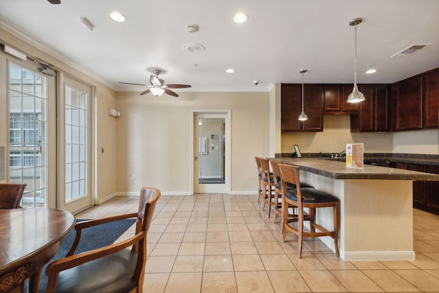 kitchen featuring light tile patterned floors, a kitchen breakfast bar, dark brown cabinets, hanging light fixtures, and ornamental molding