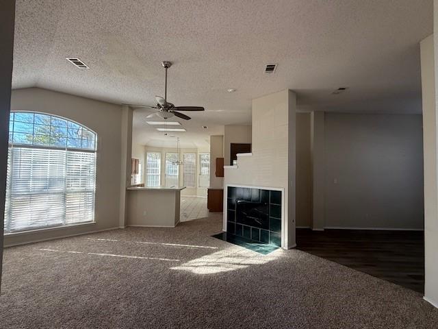 unfurnished living room featuring a tile fireplace, dark colored carpet, a textured ceiling, and ceiling fan