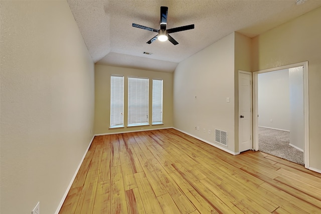 empty room featuring light wood-type flooring, a textured ceiling, lofted ceiling, and ceiling fan