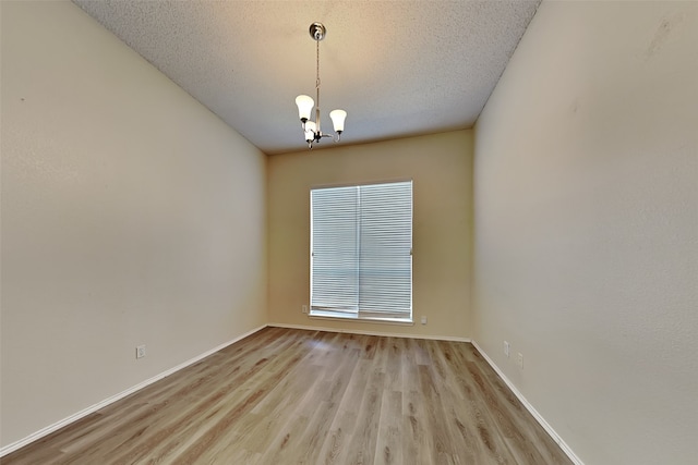 unfurnished room featuring an inviting chandelier, light hardwood / wood-style flooring, and a textured ceiling