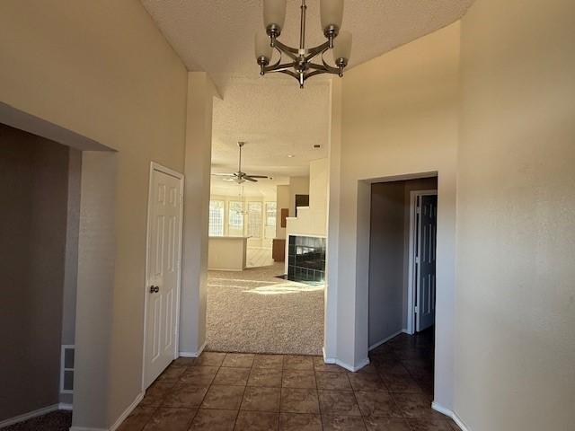 hallway with a towering ceiling, a chandelier, a textured ceiling, and dark carpet