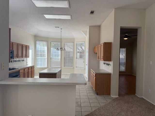 kitchen featuring pendant lighting, light tile patterned floors, a kitchen island, kitchen peninsula, and a chandelier