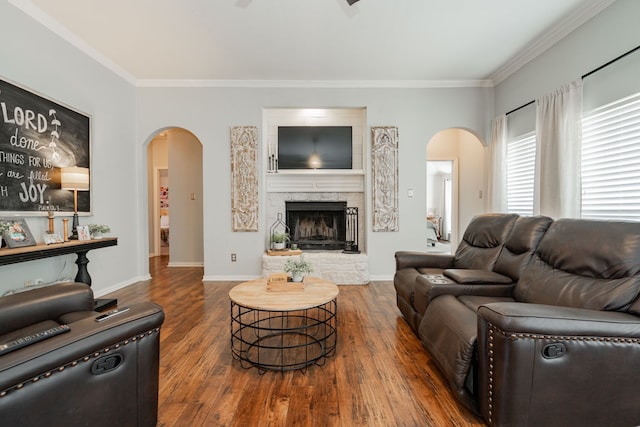 living room with dark wood-type flooring, a stone fireplace, and ornamental molding