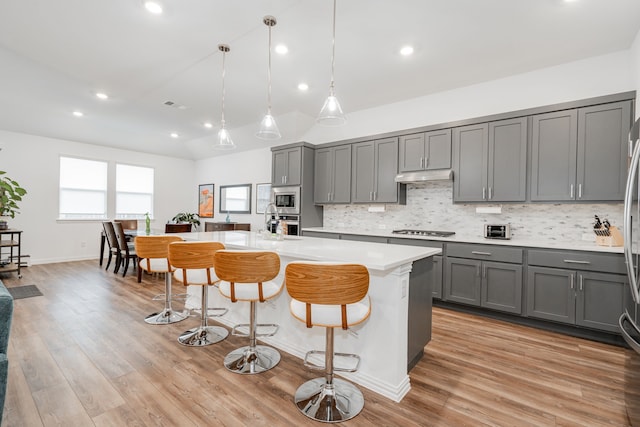 kitchen with a kitchen island, pendant lighting, a breakfast bar area, gray cabinetry, and stainless steel appliances