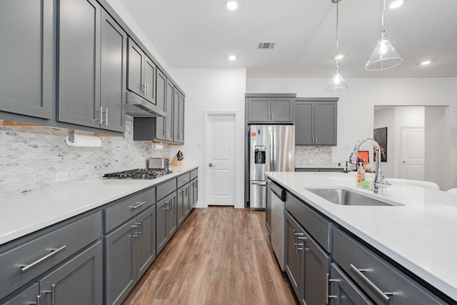 kitchen featuring appliances with stainless steel finishes, sink, gray cabinetry, hanging light fixtures, and hardwood / wood-style flooring