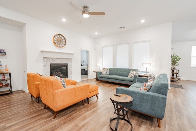 living room with ceiling fan, a tiled fireplace, and light hardwood / wood-style floors