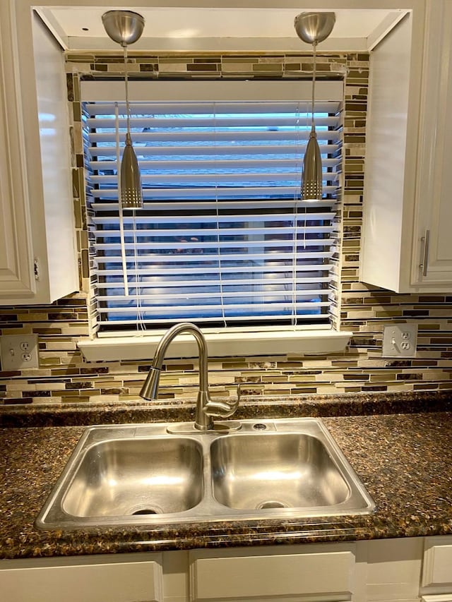 details featuring pendant lighting, white cabinets, dark stone countertops, sink, and backsplash