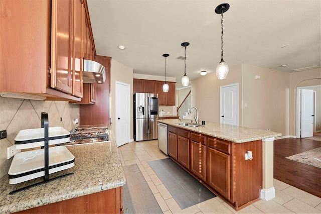 kitchen with appliances with stainless steel finishes, an island with sink, sink, hanging light fixtures, and light tile patterned floors