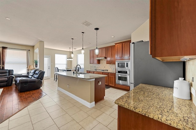 kitchen featuring light stone countertops, decorative light fixtures, stainless steel appliances, sink, and a kitchen island with sink