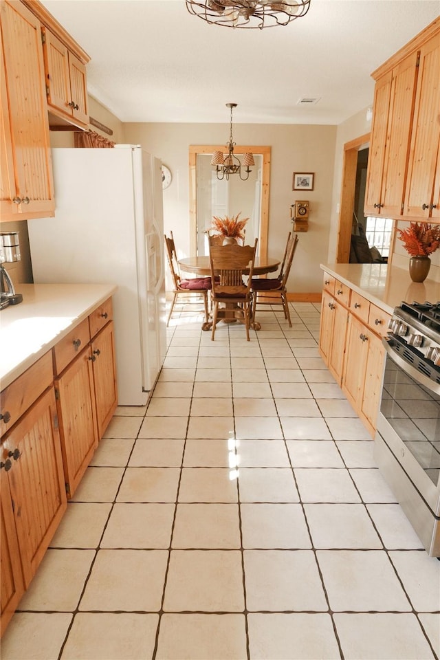 kitchen with stainless steel range with gas cooktop, hanging light fixtures, white refrigerator with ice dispenser, light tile patterned floors, and light brown cabinetry