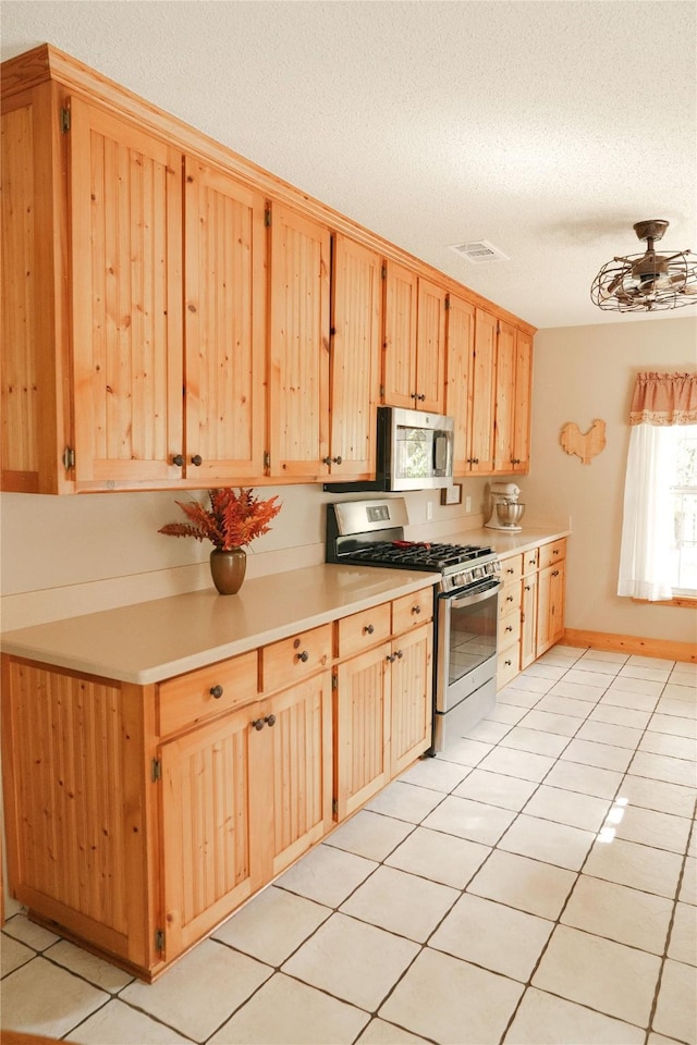 kitchen featuring ceiling fan, appliances with stainless steel finishes, light brown cabinets, a textured ceiling, and light tile patterned floors