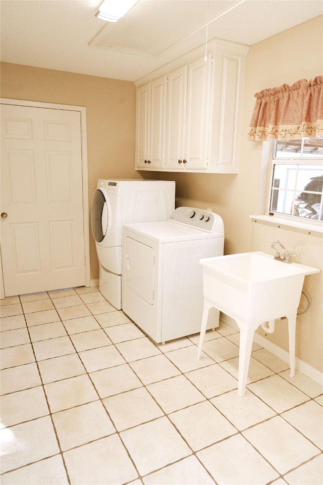 clothes washing area featuring cabinets, light tile patterned flooring, and washer and clothes dryer