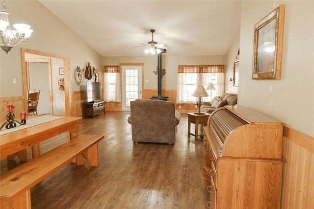 living room with lofted ceiling, dark hardwood / wood-style floors, wooden walls, a wood stove, and ceiling fan with notable chandelier