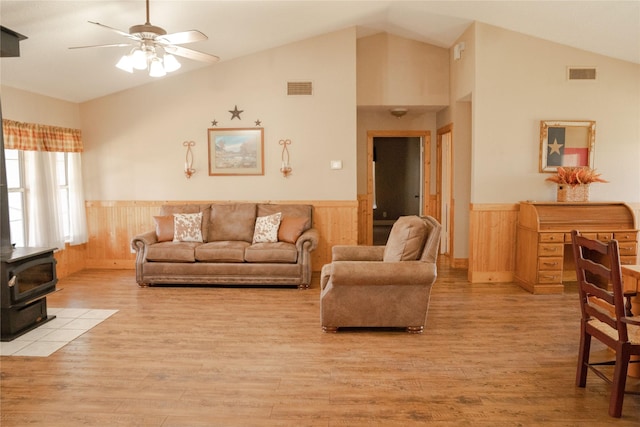 living room featuring ceiling fan, vaulted ceiling, a wood stove, and light hardwood / wood-style floors