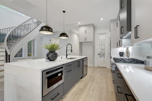 kitchen with light hardwood / wood-style flooring, decorative light fixtures, white cabinetry, sink, and a center island with sink