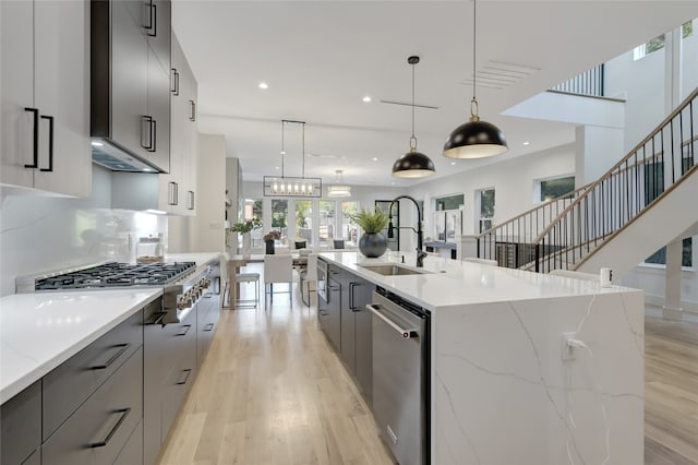 kitchen with stainless steel appliances, gray cabinetry, a large island with sink, and decorative light fixtures