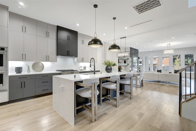 kitchen featuring gray cabinets, decorative light fixtures, a kitchen breakfast bar, a kitchen island with sink, and sink