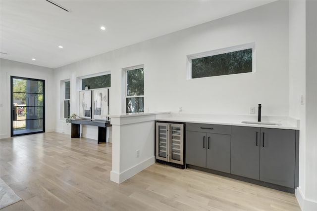 bar featuring sink, light hardwood / wood-style flooring, gray cabinets, and wine cooler