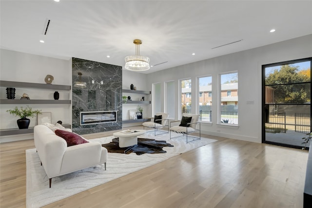 living room featuring a high end fireplace, built in features, light hardwood / wood-style flooring, and a chandelier