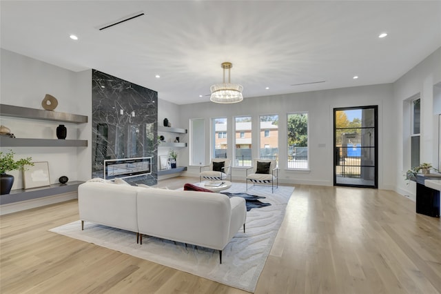 living room featuring an inviting chandelier, a high end fireplace, light hardwood / wood-style floors, and built in features