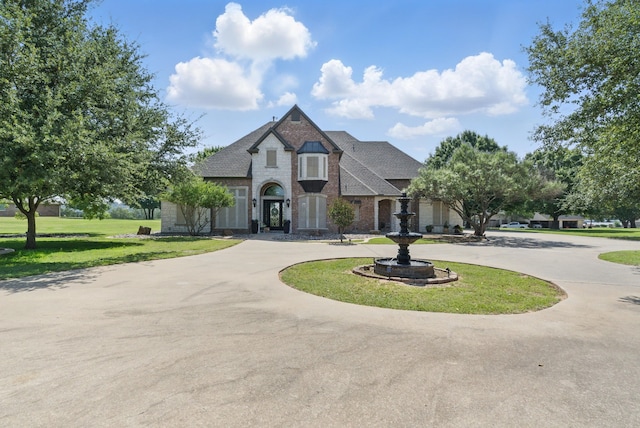 1901 Yucatan Dr, Granbury, TX 76048 - french country style house with curved driveway, a front yard, brick siding, and a shingled roof