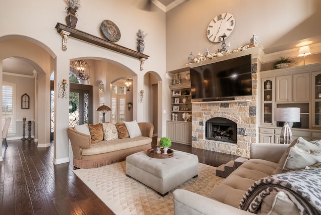 living room featuring a towering ceiling, wood-type flooring, ornamental molding, and a stone fireplace