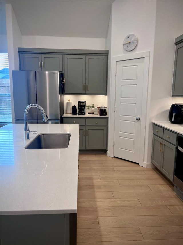 kitchen featuring sink, gray cabinetry, tasteful backsplash, light hardwood / wood-style flooring, and stainless steel refrigerator