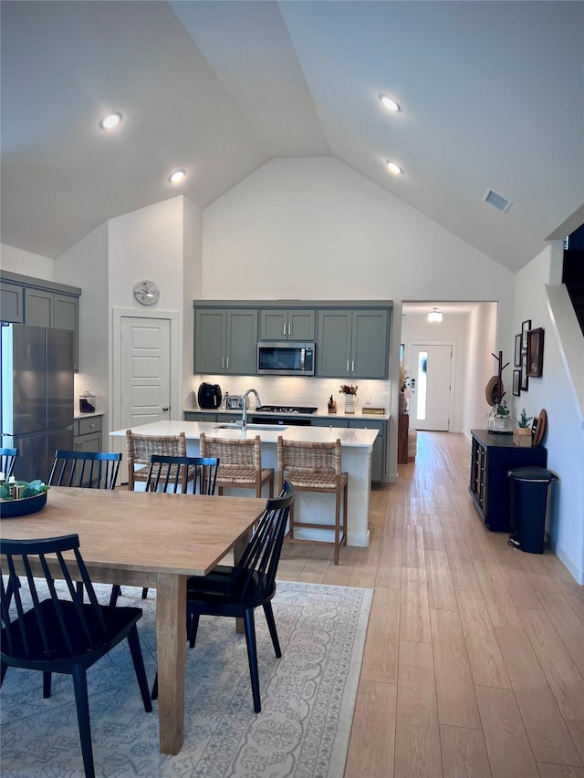 dining space with high vaulted ceiling, light hardwood / wood-style floors, and sink