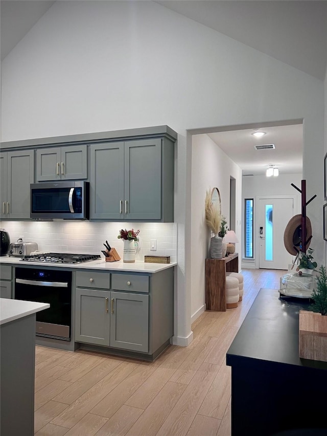 kitchen with tasteful backsplash, gray cabinetry, stainless steel appliances, and light wood-type flooring